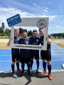 Vier Fußballspieler posieren mit einem großen Rahmen und einem Schild in der Hand.