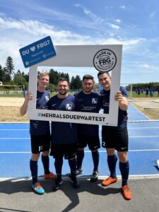 Vier Fußballspieler posieren zusammen mit einem großen Rahmen, der den Hashtag '#MEHRALSDUERWARTEST' zeigt.