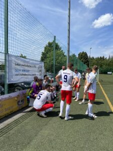 Fußballmannschaft in weißen und roten Trikots sitzt auf dem Boden und bespricht sich auf dem Spielfeld.