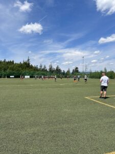 Gruppentraining auf einem Fußballfeld mit Spielern und Trainern unter blauem Himmel.