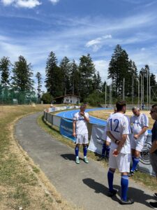 Fußballspieler in blauen Trikots stehen an einem Sportplatz und unterhalten sich.