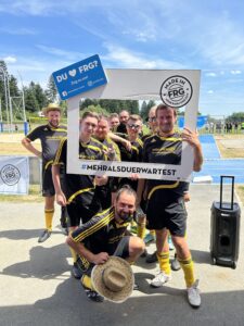 Eine Gruppe von Fußballspielern posiert mit einem großen Rahmen und einem Plakat auf einem Sportplatz.