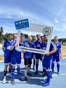 Eine Gruppe von Fußballspielern posiert mit einem großen Rahmen auf einem Sportplatz.