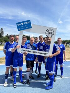 Eine Gruppe von Fußballspielern in blauen Trikots posiert mit einem großen Rahmen für ein Foto.