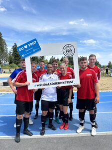 Eine Gruppe von Fußballspielern in roten Trikots posiert mit einem großen Rahmen für ein Foto.
