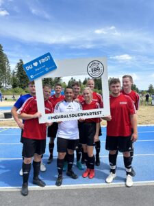 Eine Gruppe von Fußballspielern posiert mit einem großen Rahmen, der den Hashtag '#MEHRALSDUERWARTEST' zeigt.