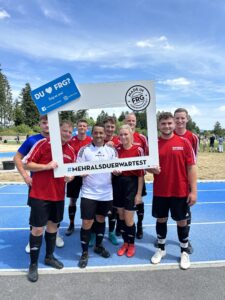 Eine Gruppe von sieben Fußballspielern in roten Trikots posiert mit einem Rahmen für ein Foto.
