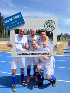Vier Fußballspieler posieren in einem Rahmen mit dem Text 'DU ♥ FRG? Zeig es uns!'.