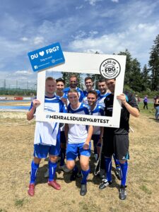 Eine Gruppe von Fußballspielern posiert mit einem großen Rahmen, der den Text 'DU ♥ FRG' enthält.