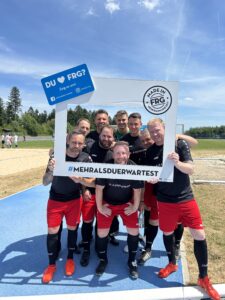 Eine Gruppe von Fußballspielern posiert mit einem großen Rahmen, der den Text 'DU ♥ FRG?' zeigt.