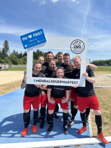 Eine Gruppe von Fußballspielern posiert mit einem großen Rahmen, der den Text 'DU ? FRG' zeigt.