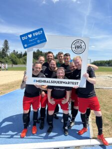 Eine Gruppe von Fußballspielern posiert mit einem großen Rahmen und einem Schild bei einem Sportevent.