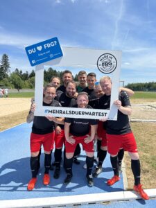 Eine Gruppe von Fußballspielern posiert mit einem großen Rahmen auf einem Sportplatz.