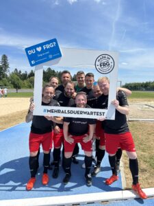 Eine Gruppe von acht Fußballspielern posiert mit einem großen Rahmen, der den Text 'DU ♥ FRG' zeigt.