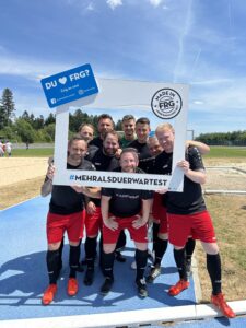 Eine Gruppe von Fußballspielern posiert mit einem großen Rahmen, der den Text 'DU ♥ FRG?' zeigt.