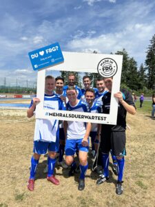 Eine Gruppe von sieben Fußballspielern posiert mit einem großen Rahmen auf einem Spielfeld.