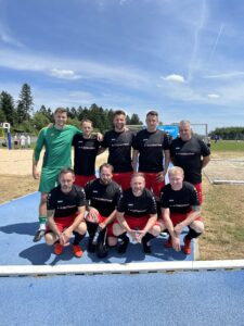 Eine Fußballmannschaft in schwarzen und roten Trikots posiert auf einem Sportplatz.