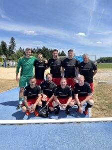 Eine Fußballmannschaft in schwarzen und roten Trikots posiert auf einem Sportplatz.