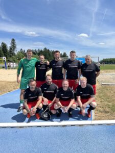Eine Fußballmannschaft in schwarzen und roten Trikots posiert auf dem Spielfeld nach einem Spiel.