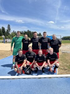 Eine Fußballmannschaft in schwarzen und roten Trikots posiert auf einem Sportplatz.