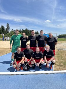 Eine Fußballmannschaft in schwarzen Trikots mit roten Hosen auf einem Sportplatz im Freien.