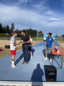 Ein Fußballspieler in rot-weißer Kleidung erhält eine Auszeichnung von einem Mann in schwarzem Hemd während einer Zeremonie.