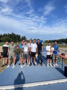 Gruppe von Männern und einer Frau mit einem Kind, die eine Urkunde auf einem Sportplatz halten.