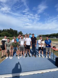 Eine Gruppe von Personen posiert auf einem Sportplatz, einige halten ein Zertifikat und ein Kind.