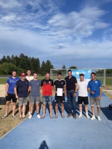 Eine Gruppe von Fußballspielern und Trainern steht auf einem Sportplatz, einige halten ein Zertifikat.