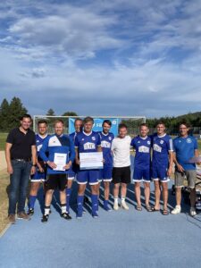 Eine Fußballmannschaft in blauen Trikots posiert für ein Gruppenfoto auf dem Spielfeld.