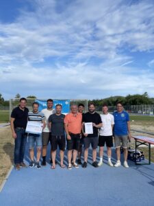Gruppe von Sportlern posiert mit einer Auszeichnung und einem Scheck auf einem Sportplatz.