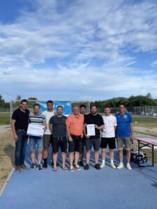 Eine Gruppe von Sportlern posiert für ein Foto mit Urkunden und einem Scheck im Freien.