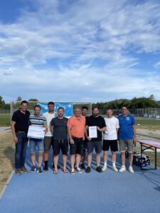 Eine Gruppe von acht Personen steht zusammen und hält Urkunden bei einer Sportveranstaltung im Freien.