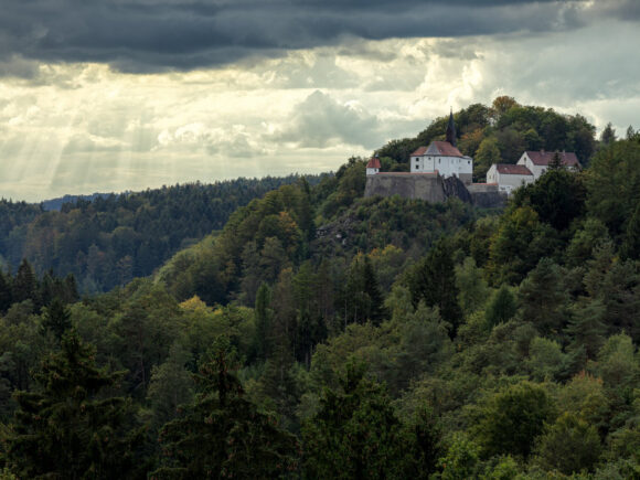 Burg Ranfels auf einem Hügel, umgeben von Bäumen und bewölktem Himmel.