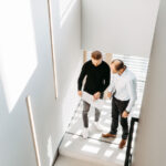 Zwei Männer betrachten einen Plan in einem modernen Treppenhaus mit Lichtstrahlen.