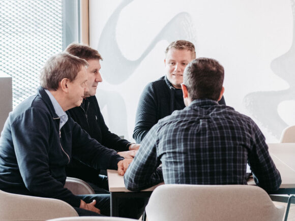 Vier Männer sitzen an einem Tisch und diskutieren in einem modernen Raum.