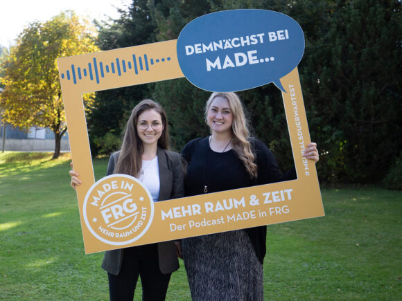 Zwei Frauen halten einen großen Rahmen mit dem Schriftzug 'Demnächst bei MADE...' und dem Logo des Podcasts MADE in FRG.