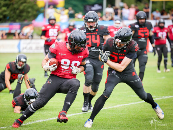Ein American Football Spieler in rotem Trikot mit der Nummer 90, der von einem anderen Spieler verfolgt wird.