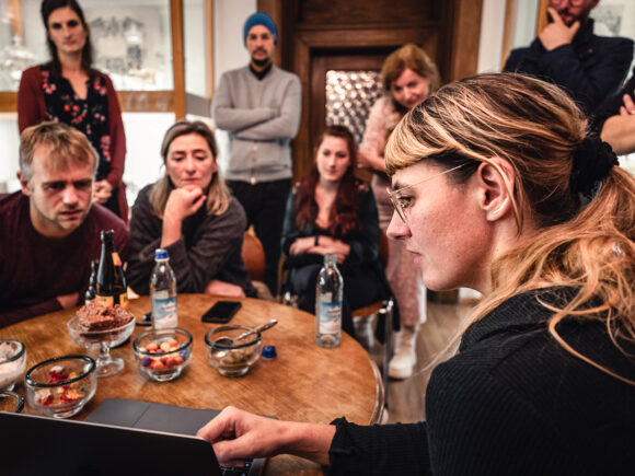 Eine Gruppe von Menschen schaut auf einen Laptop während einer Besprechung an einem Tisch.