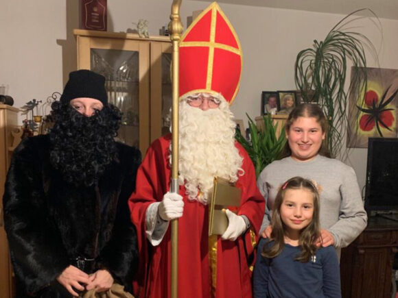 Nikolaus in rotem Gewand mit zwei Kindern und einer Person mit schwarzem Bart.