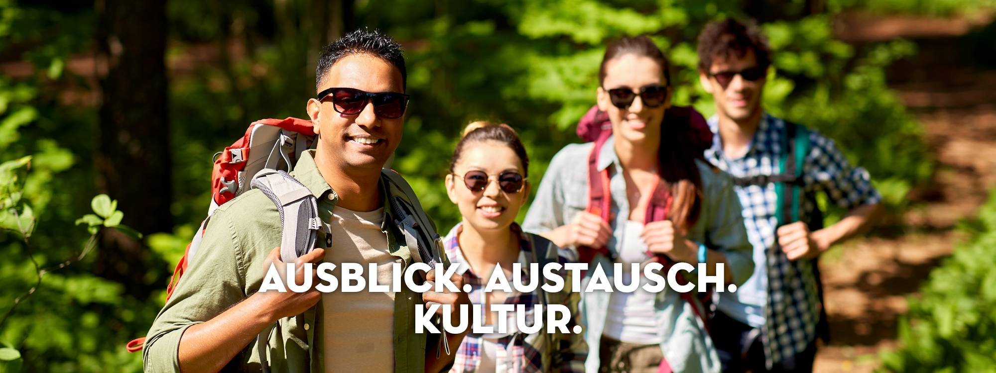 Vier Wanderer im Freien, die in die Kamera lächeln und Rucksäcke tragen.