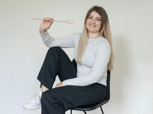 Eine Frau sitzt auf einem Stuhl und hält einen Holzlöffel in der Hand.