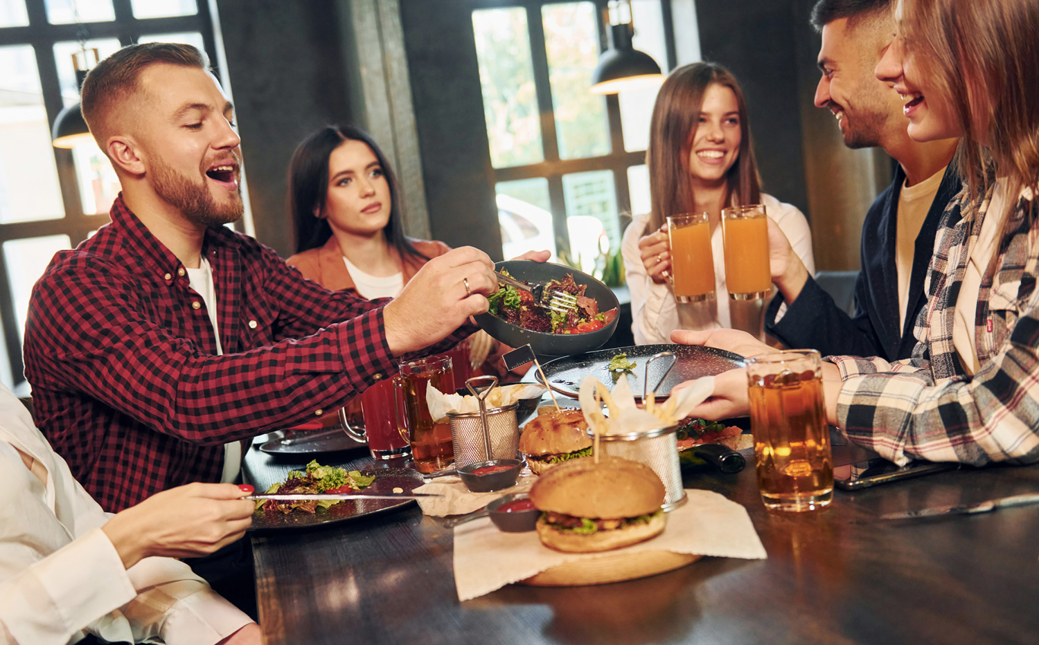 Vier Freunde genießen gemeinsam einen Restaurantabend mit Burgern, Salat und Getränken bei der MADE Gastro-Tour im Landkreis Freyung-Grafenau.