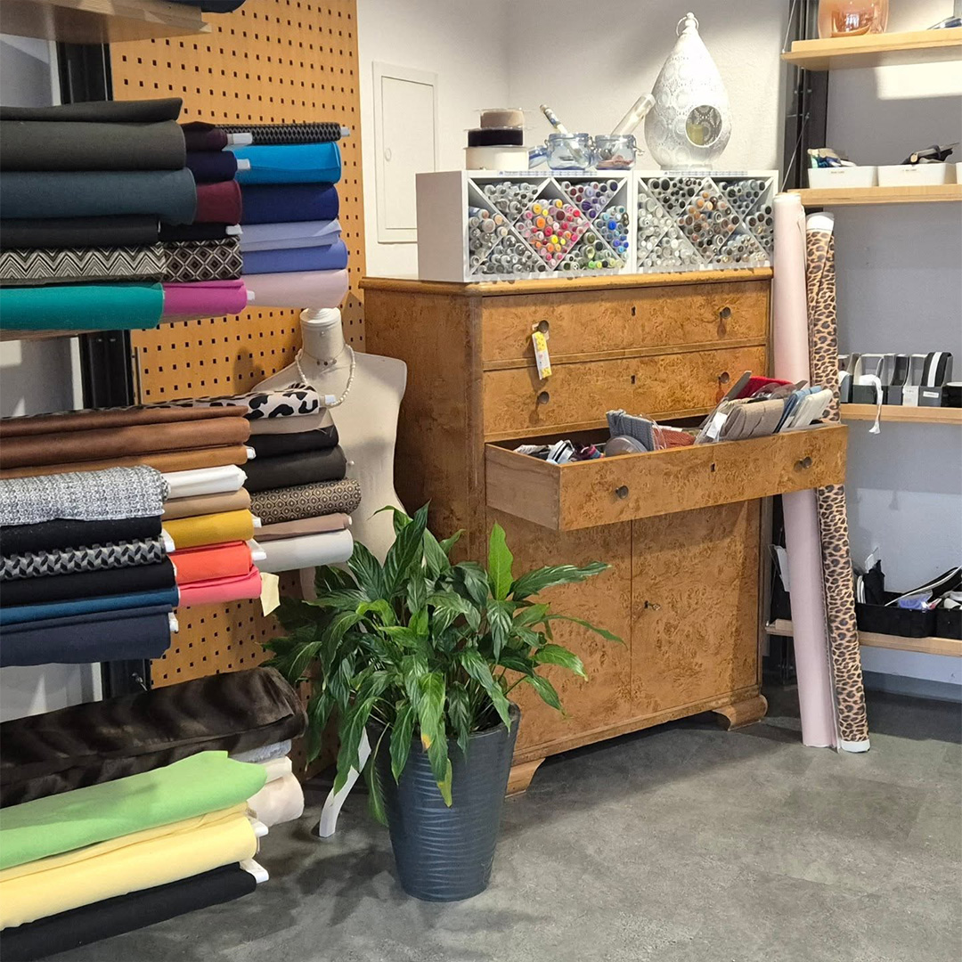 Bunte Stoffrollen, Schneiderei-Werkstatt und Stoffauswahl bei Knopfloch Stoffe & Änderungsschneiderei: Mannequin, Schubladen und grüne Deko.