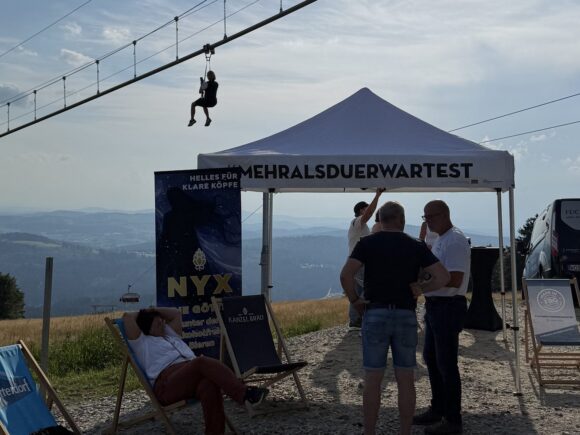 Bei einem Afterwork am Almberg schwebt ein Gast auf der Flyline über dem Treffpunkt mit NYX-Bierstand und Fernblick ins Tal.
