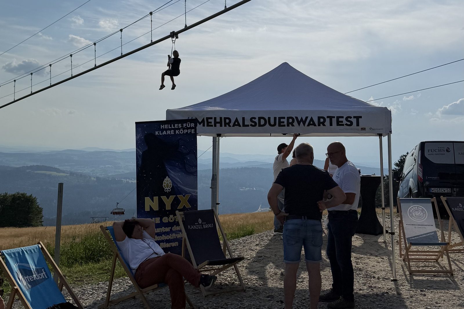 Bei einem Afterwork am Almberg schwebt ein Gast auf der Flyline über dem Treffpunkt mit NYX-Bierstand und Fernblick ins Tal.