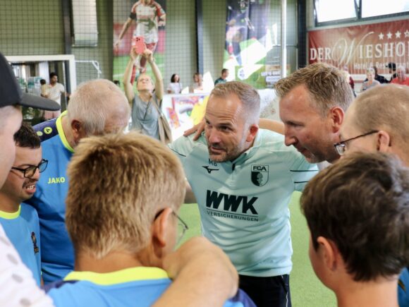Beim inklusiven Fußballtraining bilden Manuel Baum und Spieler der Bolzrebellen einen Teamkreis in der Halle von Spiegelau.