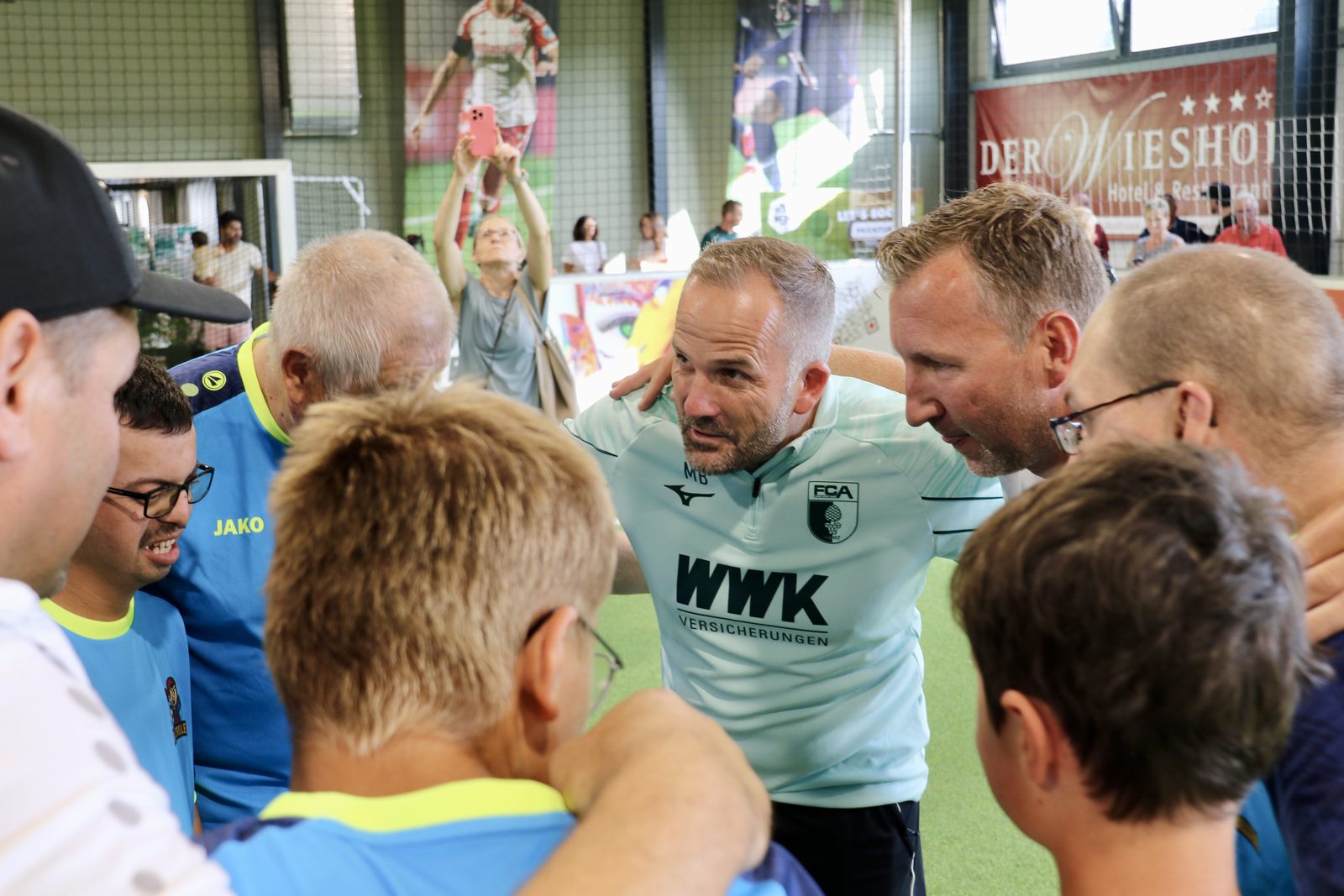 Beim inklusiven Fußballtraining bilden Manuel Baum und Spieler der Bolzrebellen einen Teamkreis in der Halle von Spiegelau.
