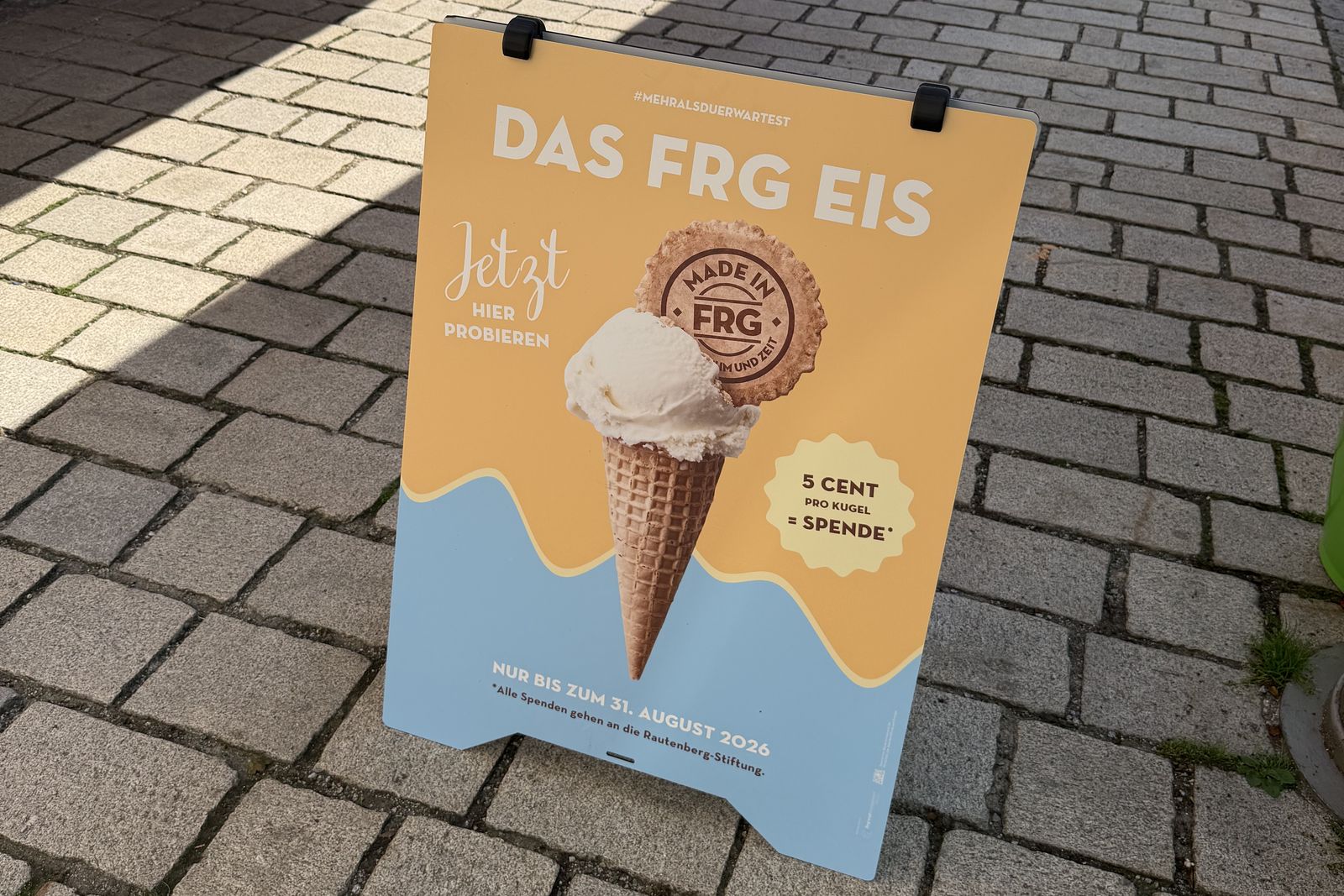 Ein Aufsteller wirbt mit „DAS FRG EIS“ und zeigt eine Eiswaffel; pro verkaufter Kugel gehen fünf Cent an die Rautenberg-Stiftung.