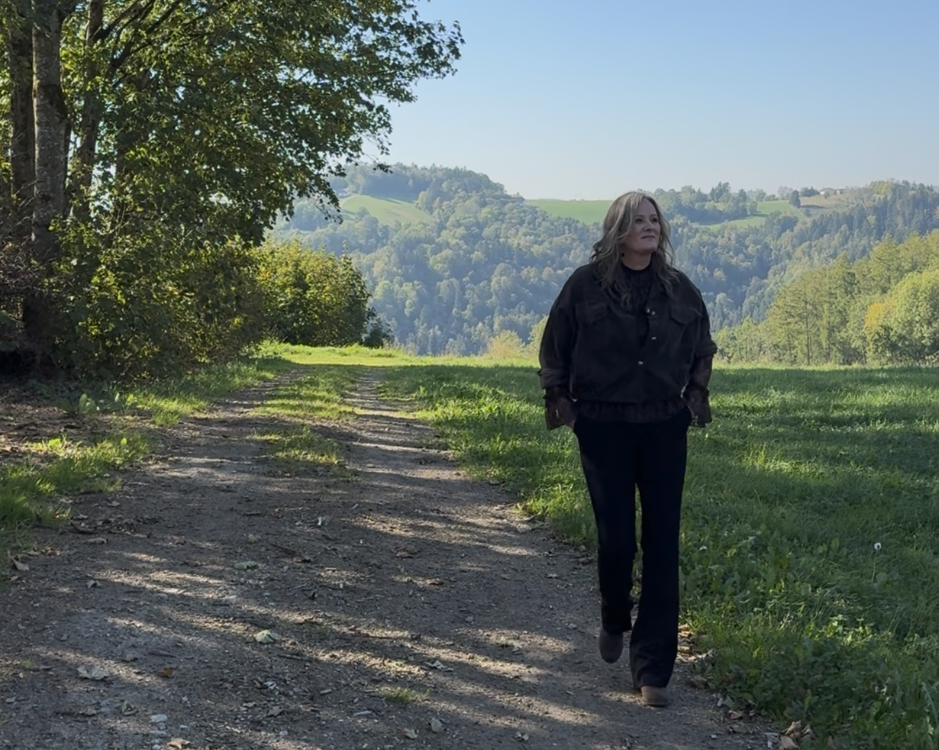 Marion Bauer geht auf einem schattigen Feldweg durch die grüne Hügellandschaft des Landkreises Freyung-Grafenau.